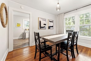 A dining area with a wooden table, black chairs, and two abstract paintings on the wall.