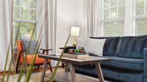 Ein Wohnzimmer mit einer Couch, einem Tisch, einer Lampe und einem Sessel.