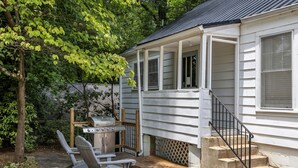 Ein Haus mit überdachter Veranda, Grill und zwei Adirondack-Stühlen.