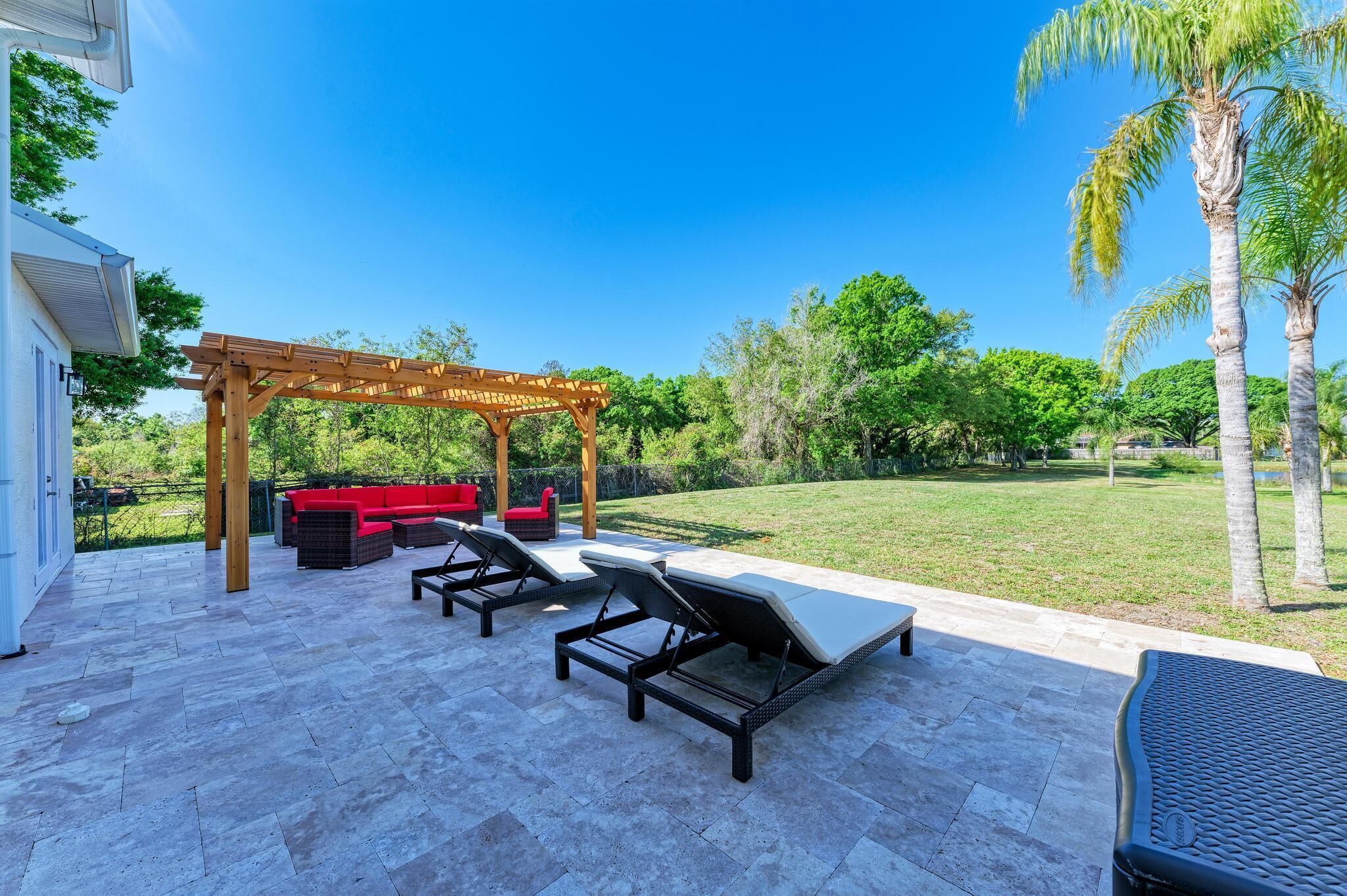 An outdoor patio with a pergola, lounge chairs, and a red sofa.