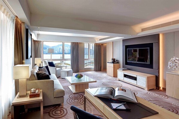A modern hotel room with a sofa, armchair, coffee table, TV, and a view of the city through large windows. - The Royal Garden Tsim Sha Tsui (Kowloon)