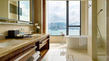 Un baño moderno con un espejo grande, un tocador de madera, una bañera y vistas a la ciudad a través de amplias ventanas.