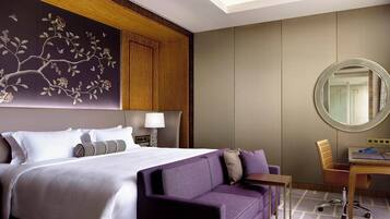 A hotel room with a large bed, a purple sofa, a desk, and a mirror.