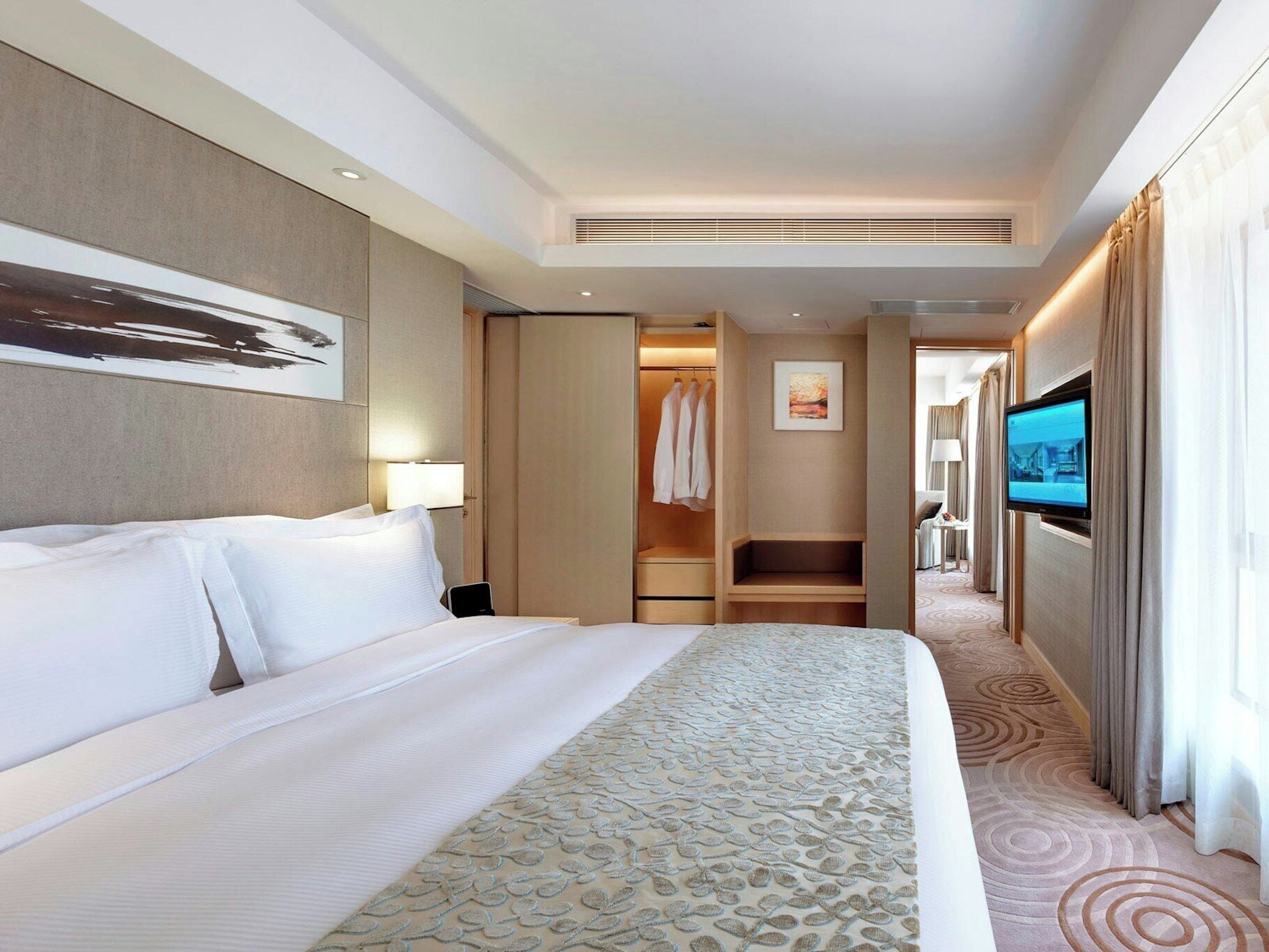 A hotel room with a large bed, a walk-in closet, a television, and a bathroom visible through an open door.