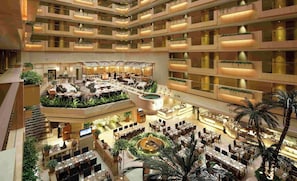 Un atrium d’hôtel à plusieurs niveaux, doté d’un élément aquatique central, de plusieurs espaces de restauration et de balcons.