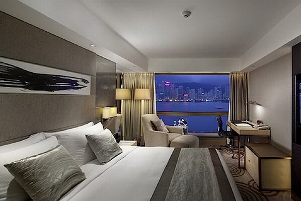 Habitación de hotel con una cama grande, un escritorio, una silla, vistas de la ciudad y un ventanal con cortinas.