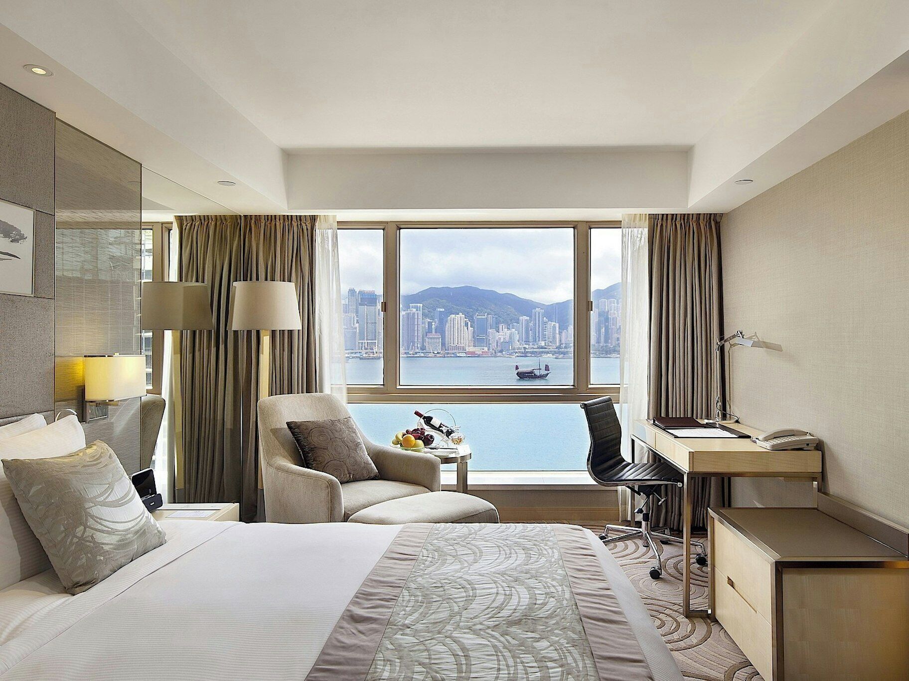 A hotel room with a bed, a desk, a chair, and a view of a cityscape.