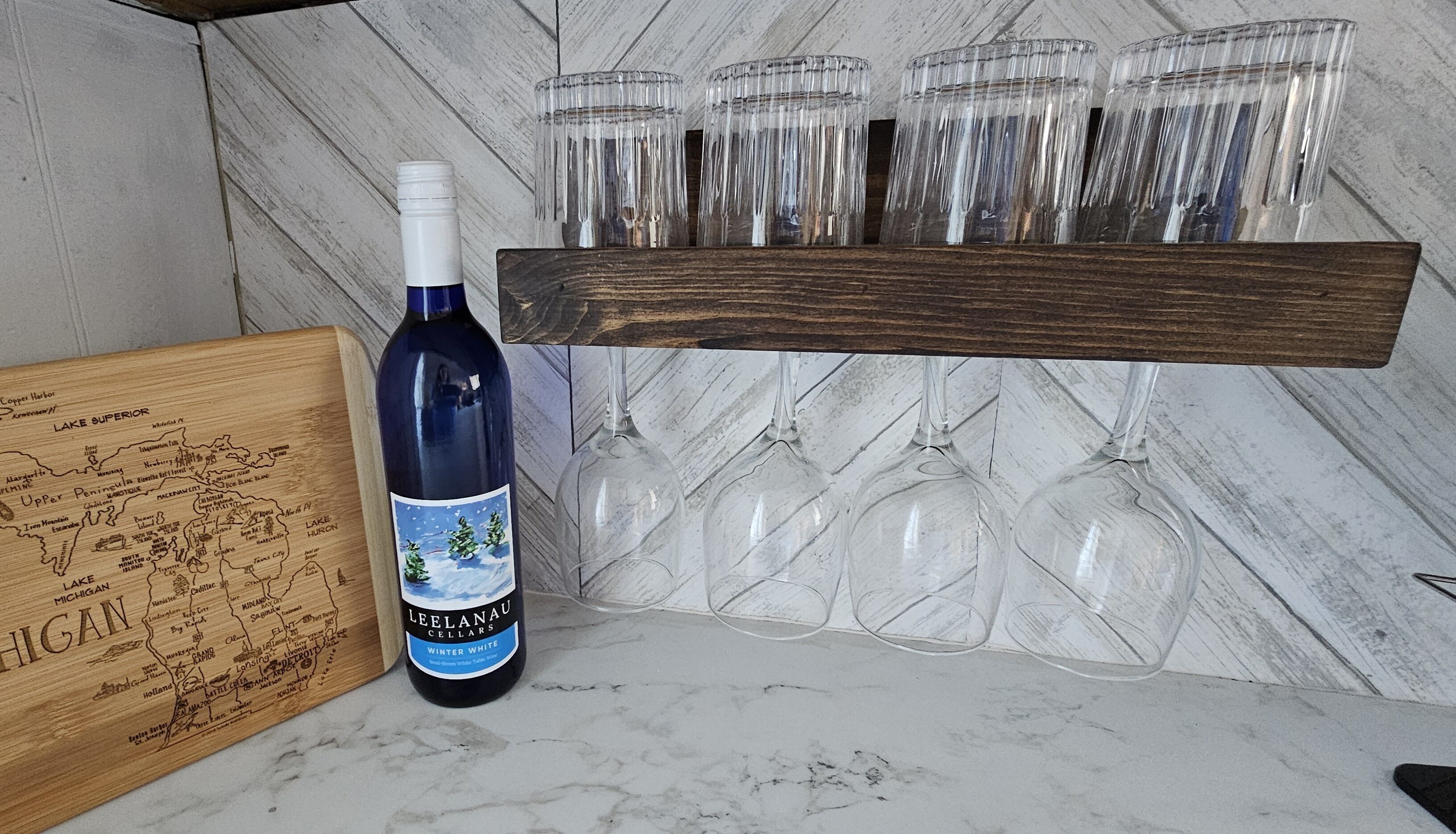 A bottle of Leelanau Cellars Winter White wine, a wooden map, and a wooden wine rack with six glasses.