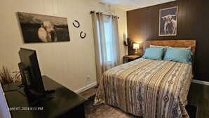 A bedroom with a bed, a TV, a nightstand, a lamp, and a window with curtains.