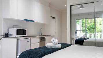A hotel room with a bed, a microwave, a small refrigerator, a sink, and a large window with a view of greenery.