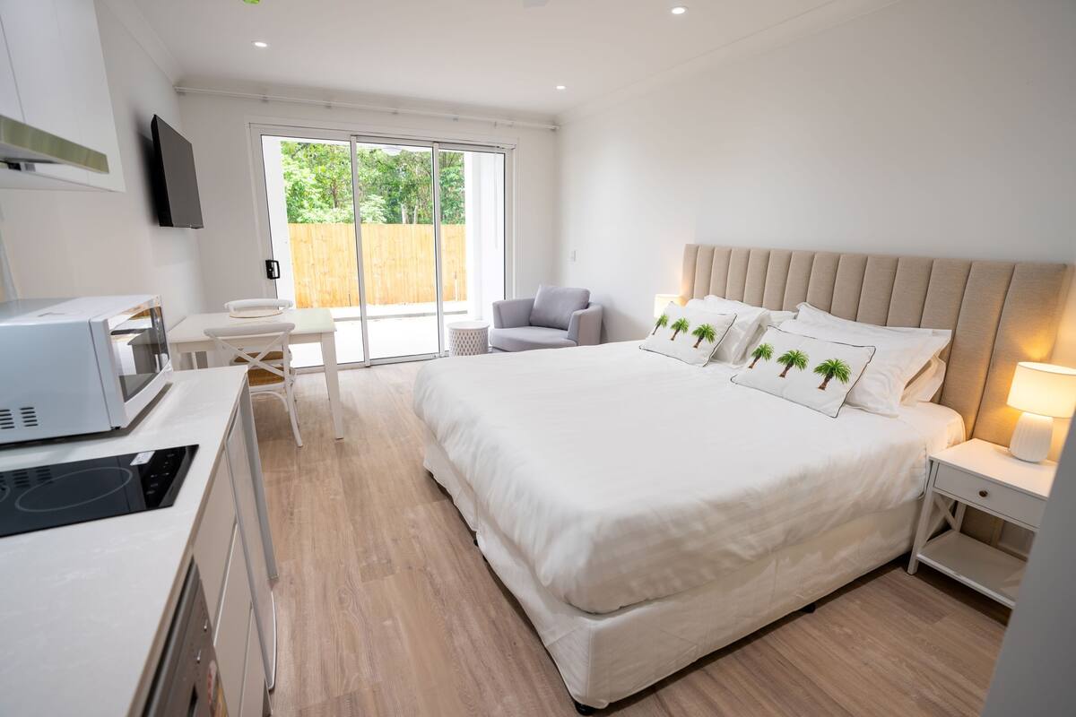 A modern bedroom with a large bed, a desk, a chair, and a TV mounted on the wall.