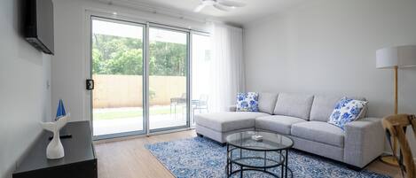 A modern living room with a grey sofa, a glass coffee table, a black side table, and a ceiling fan.