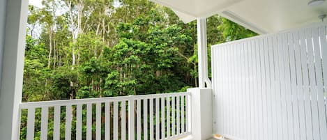 A covered balcony with white railings, a ceiling fan, and a view of a dense forest.