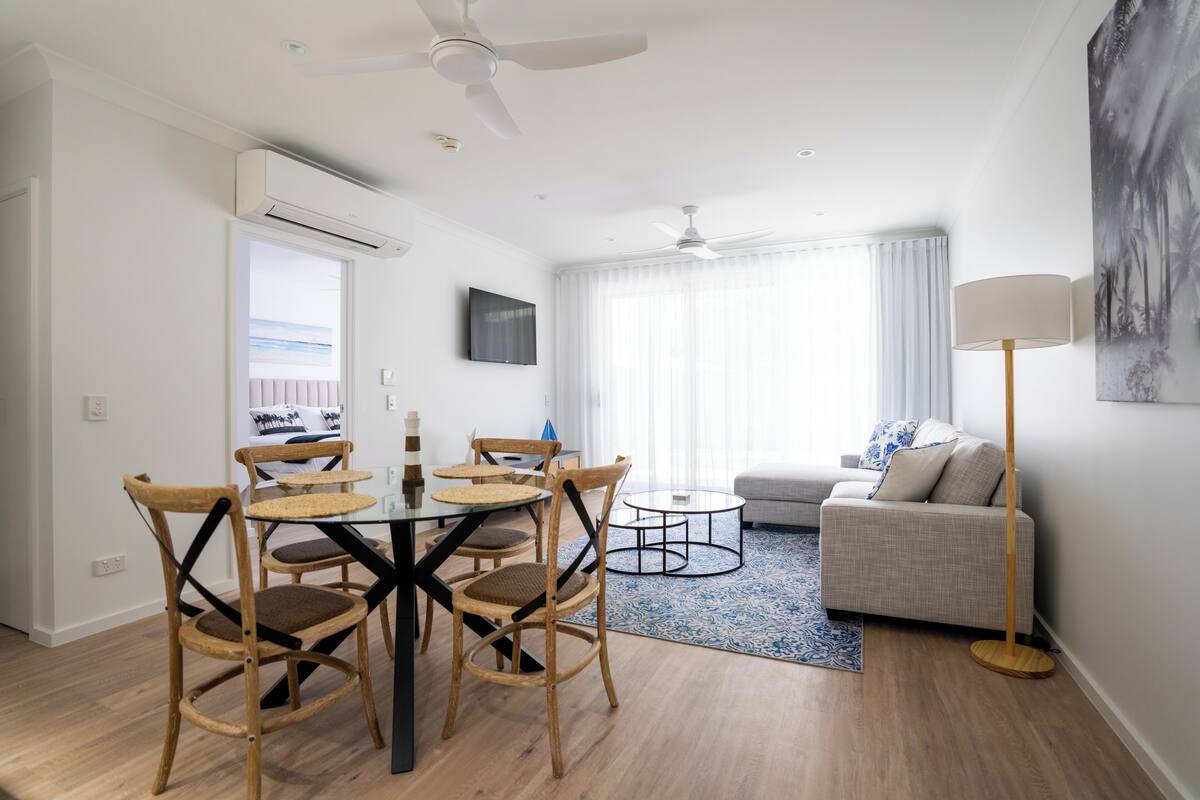 A modern living room with a sofa, a coffee table, and a dining area with chairs and a table.