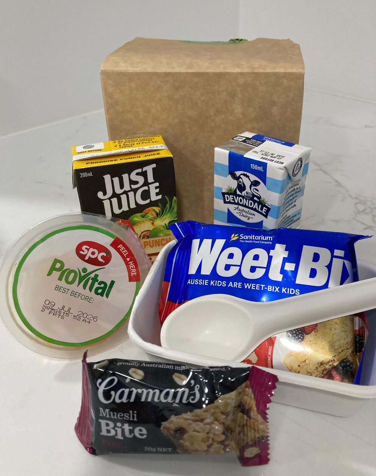 Variedad de alimentos que incluyen Just Juice, leche Devondale Dairy, yogur Pockital, Weet-Bix y Muesli Bite de Carman's.