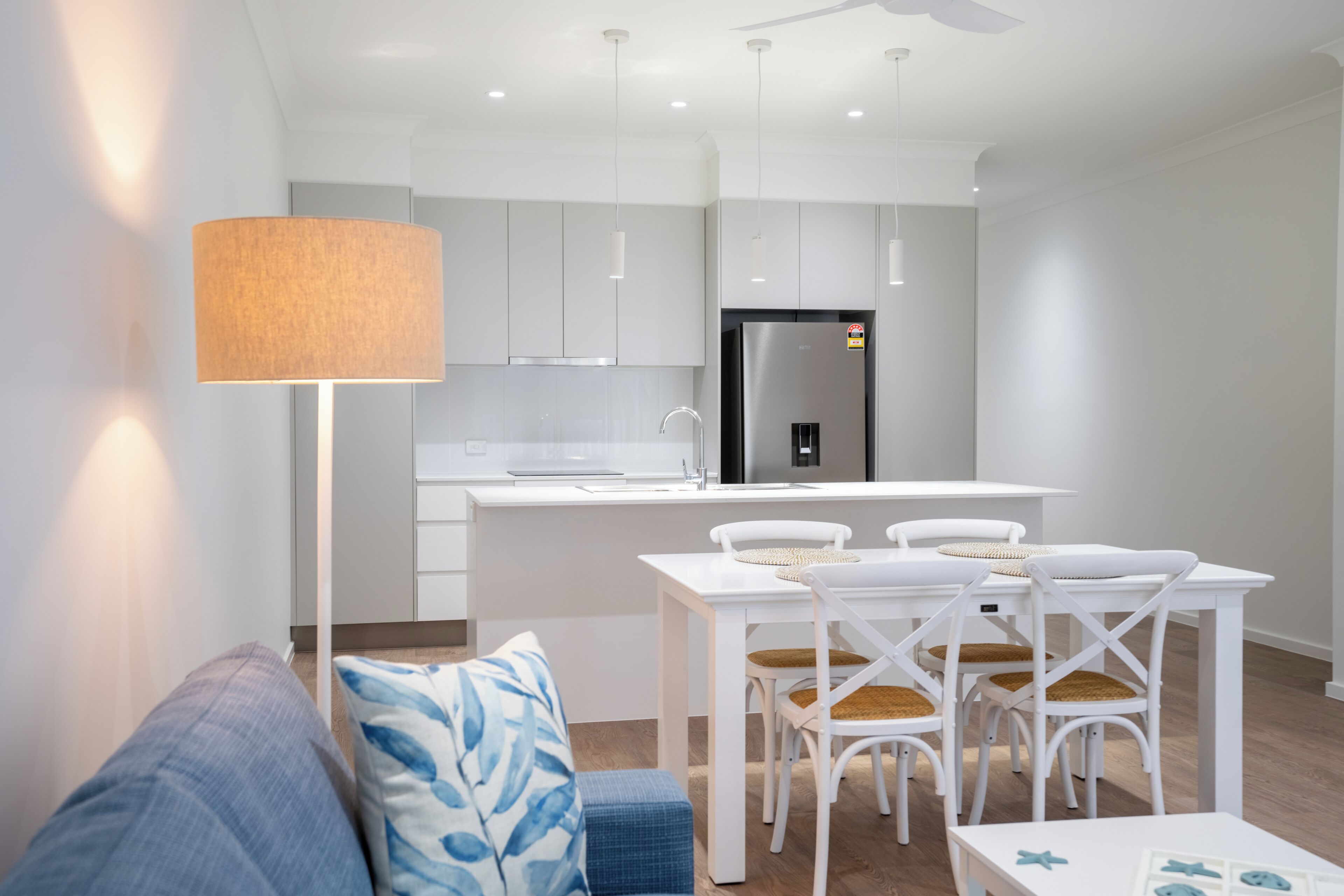 A modern kitchen with white cabinets, a stainless steel refrigerator, and a dining area with white chairs and a table.