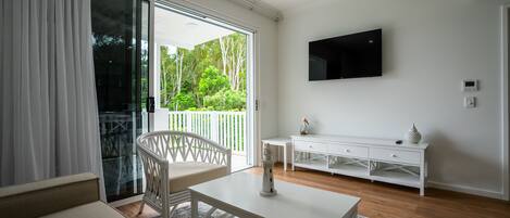 A modern living room with a white sofa, a white coffee table, a white TV stand, and a view of a balcony with greenery.