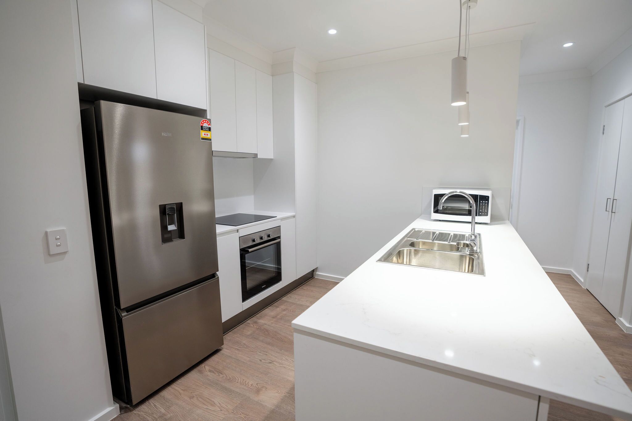 A modern kitchen with a stainless steel refrigerator, a built-in oven, a microwave, and a white countertop with a sink.