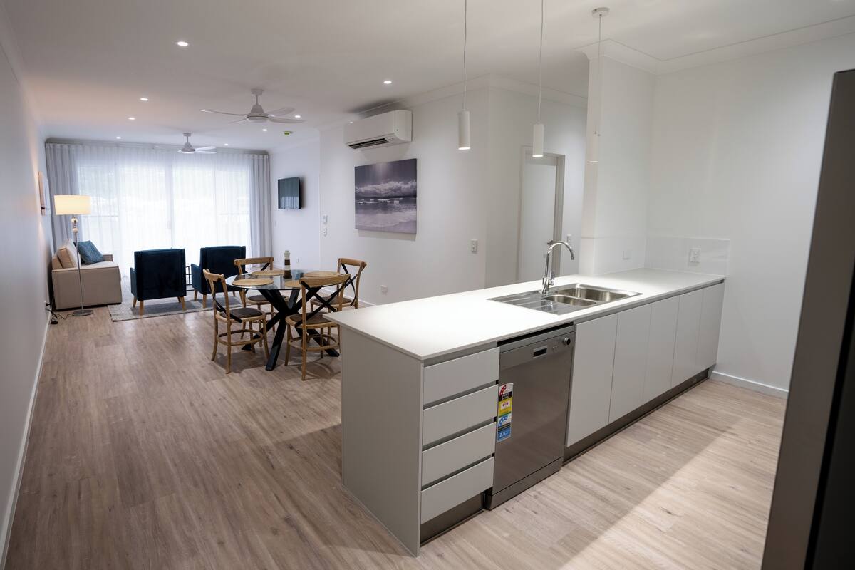 A modern kitchen with a central island, built-in dishwasher, and a large window.