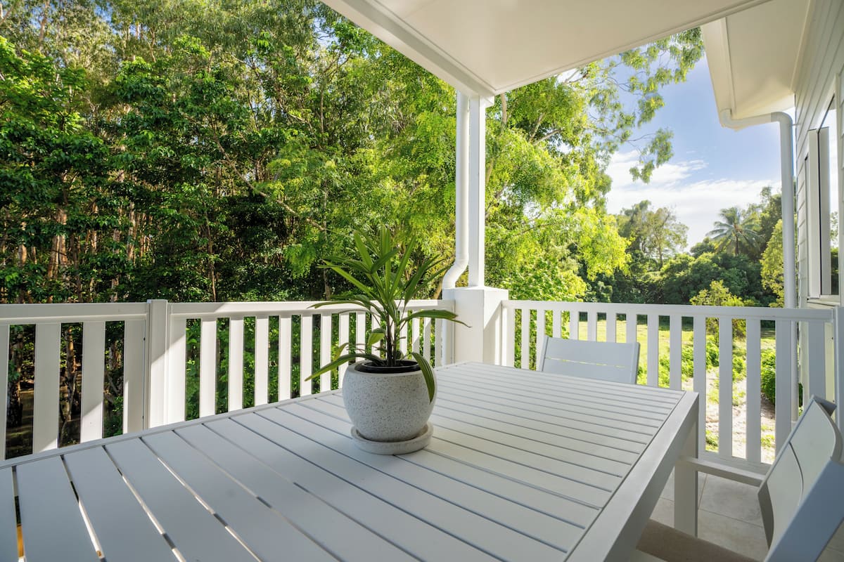 A white wooden deck with a table and chairs, surrounded by white railings, and a potted plant in the center.