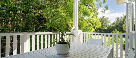 A white wooden deck with a table and chairs, surrounded by white railings, and a potted plant in the center.