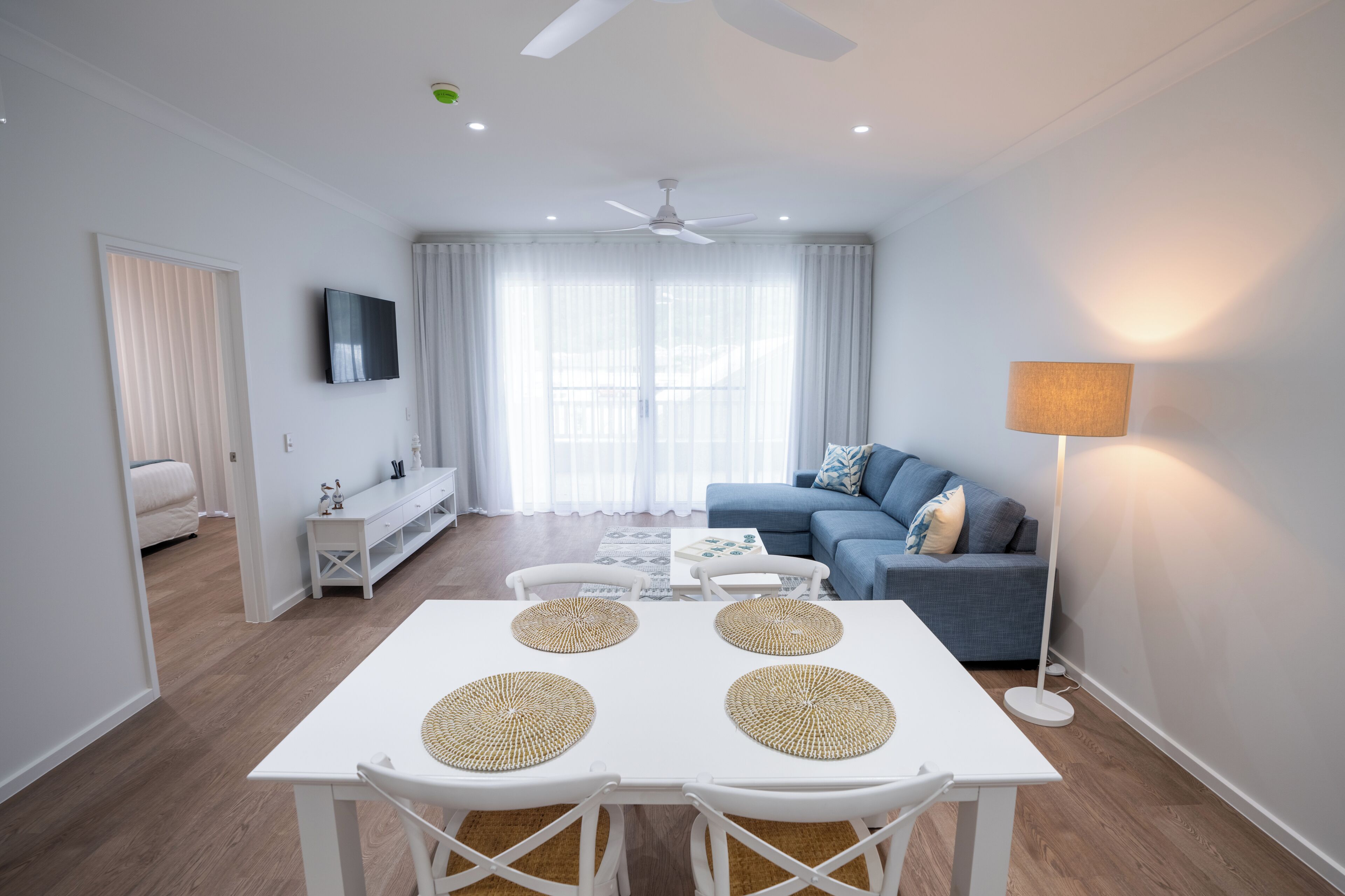 A modern living room with a white table, four chairs, a blue sofa, and a floor lamp.