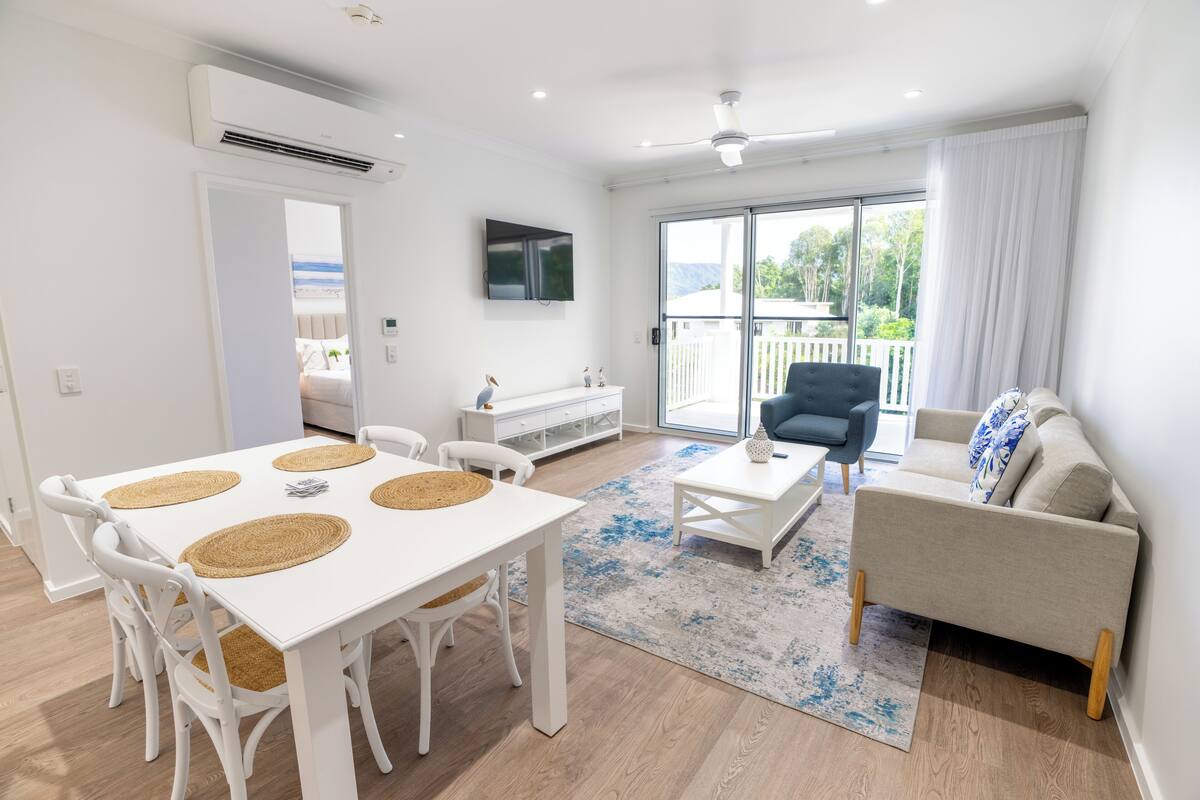 A modern living room with a white table, chairs, a sofa, and a TV.