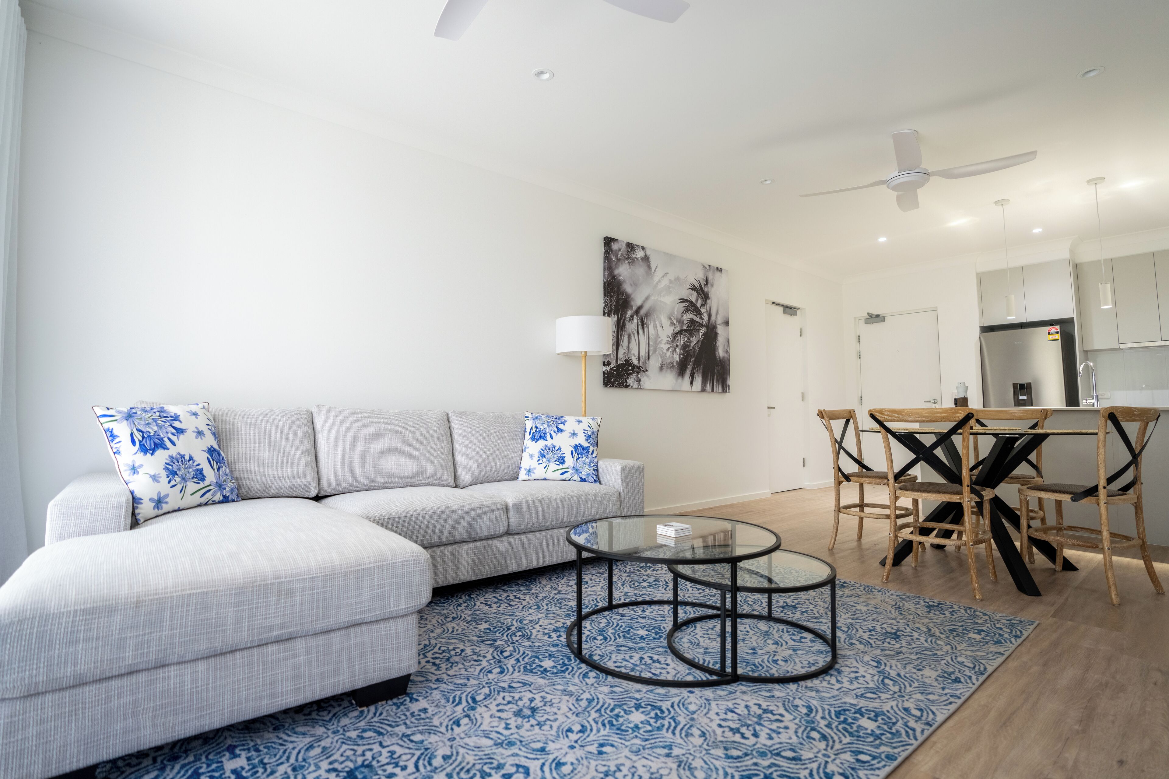 Ein modernes Wohnzimmer mit einem grauen Ecksofa, einem Glastisch und einem Essbereich mit Holzkohle-Stühlen und einem Glastisch.