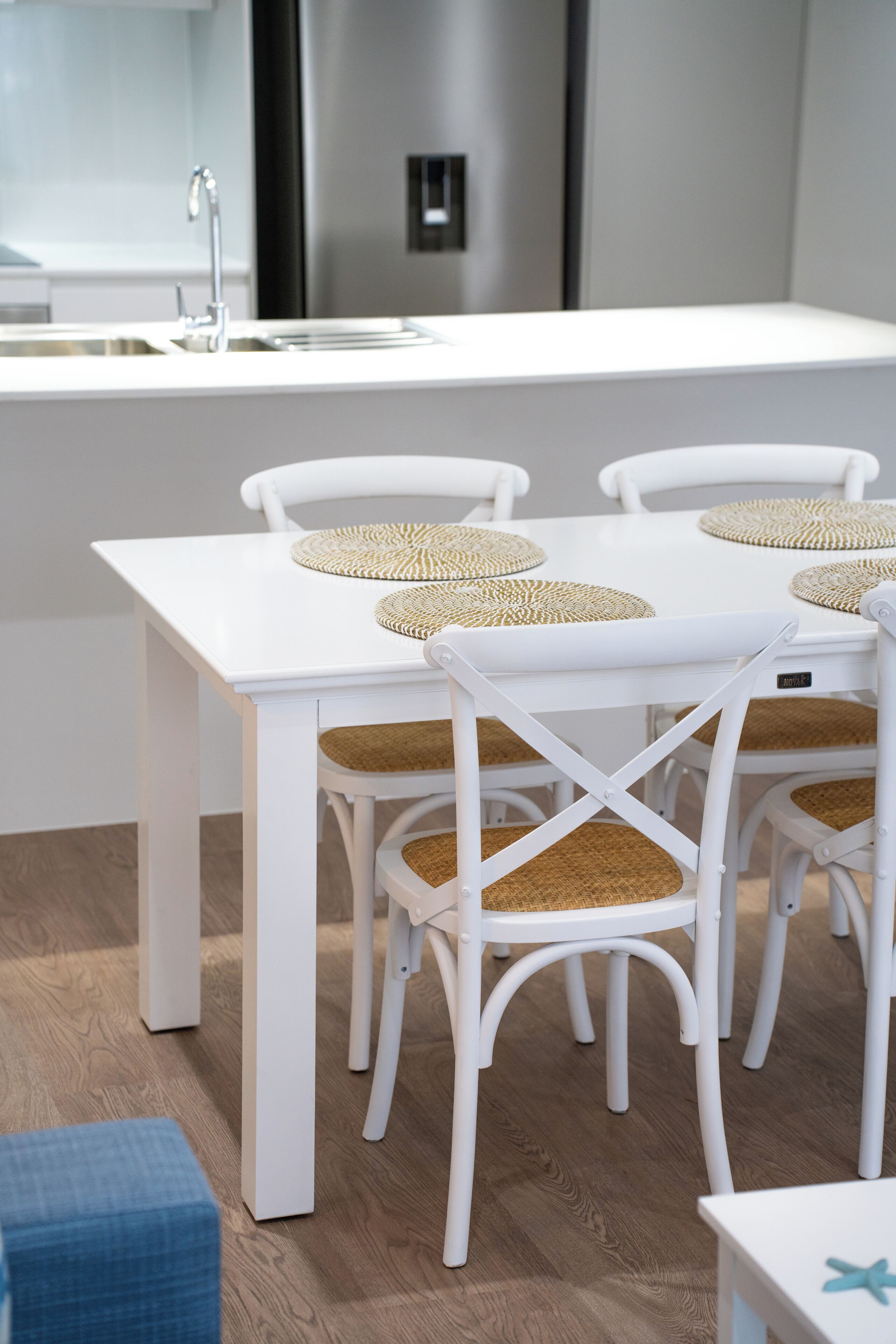 A modern kitchen with white cabinetry, a stainless steel refrigerator, and a white dining table with woven placemats.