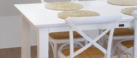 A modern kitchen with white cabinetry, a stainless steel refrigerator, and a white dining table with woven placemats.