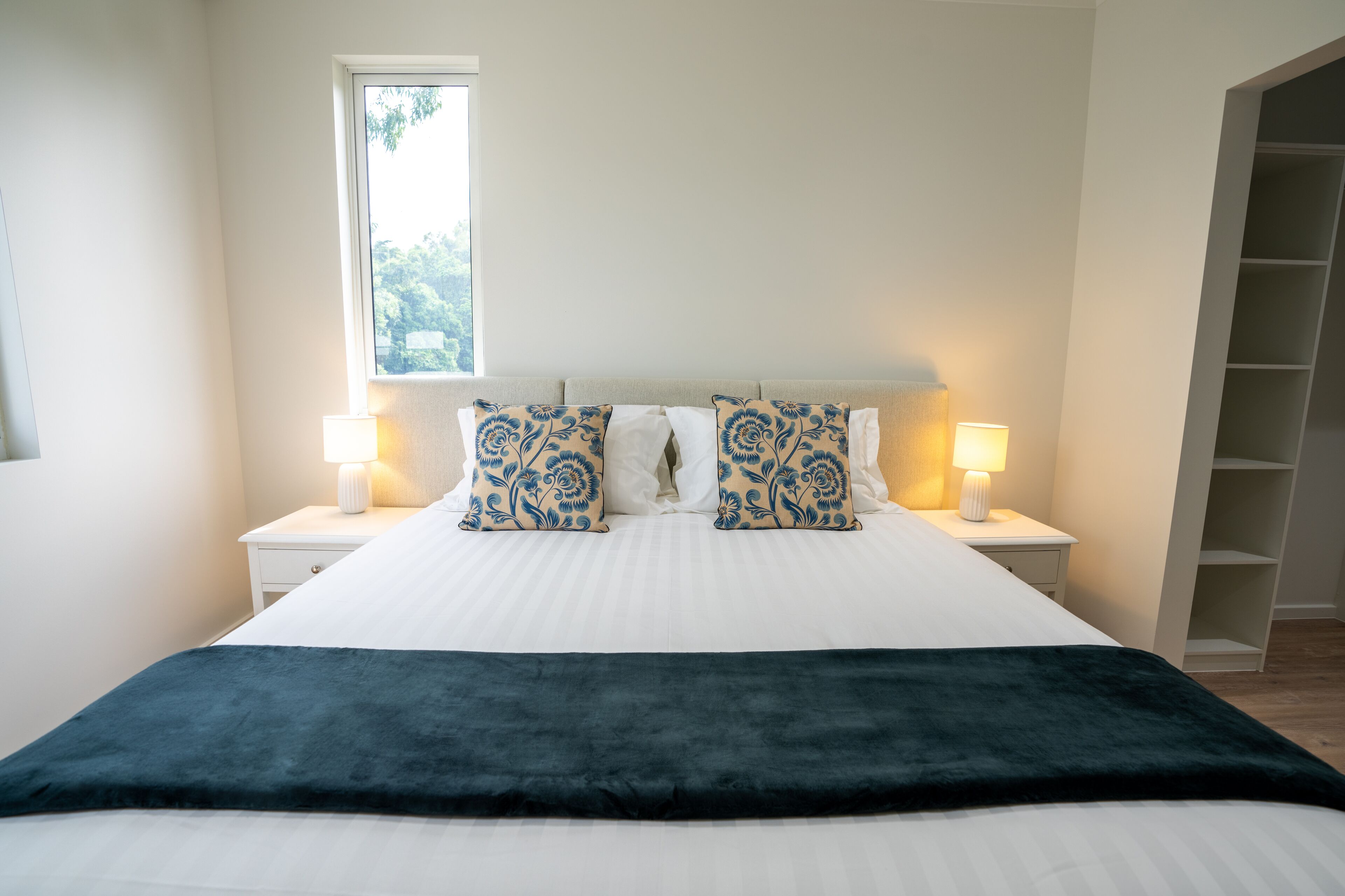 A neatly made bed with a dark throw blanket, two matching pillows, and two bedside lamps.