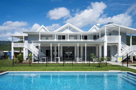 A large, white, two-story house with a swimming pool in front.