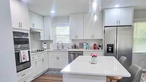 A modern kitchen with white cabinets, a central island, stainless steel appliances, and a pendant light. - Amazing Women’s and Men’s Masters Tournament Rental- Fully Remodeled. (Martinez)