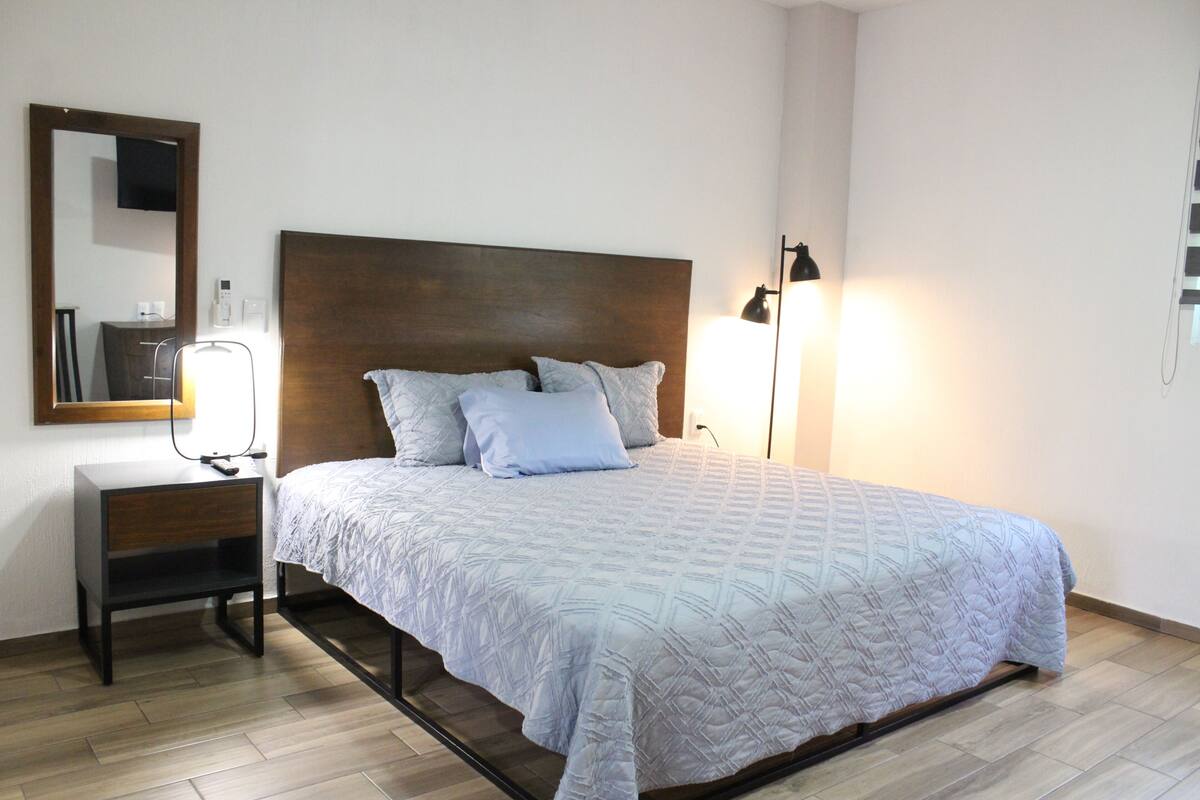 A bedroom with a bed, bedside table, lamp, and a mirror.