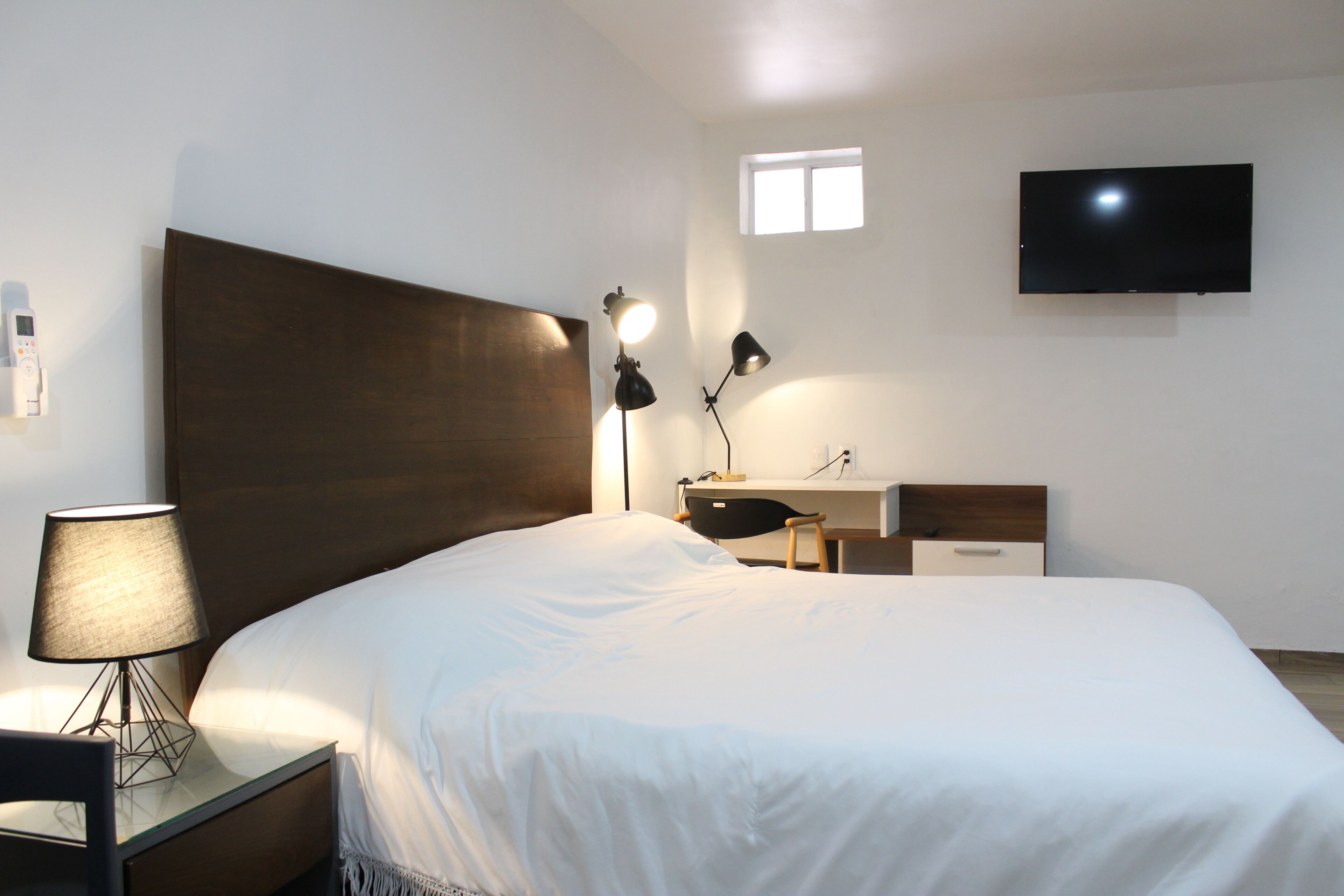 Una habitación de hotel con cama, lámparas de noche, escritorio, televisor y un ventanal.