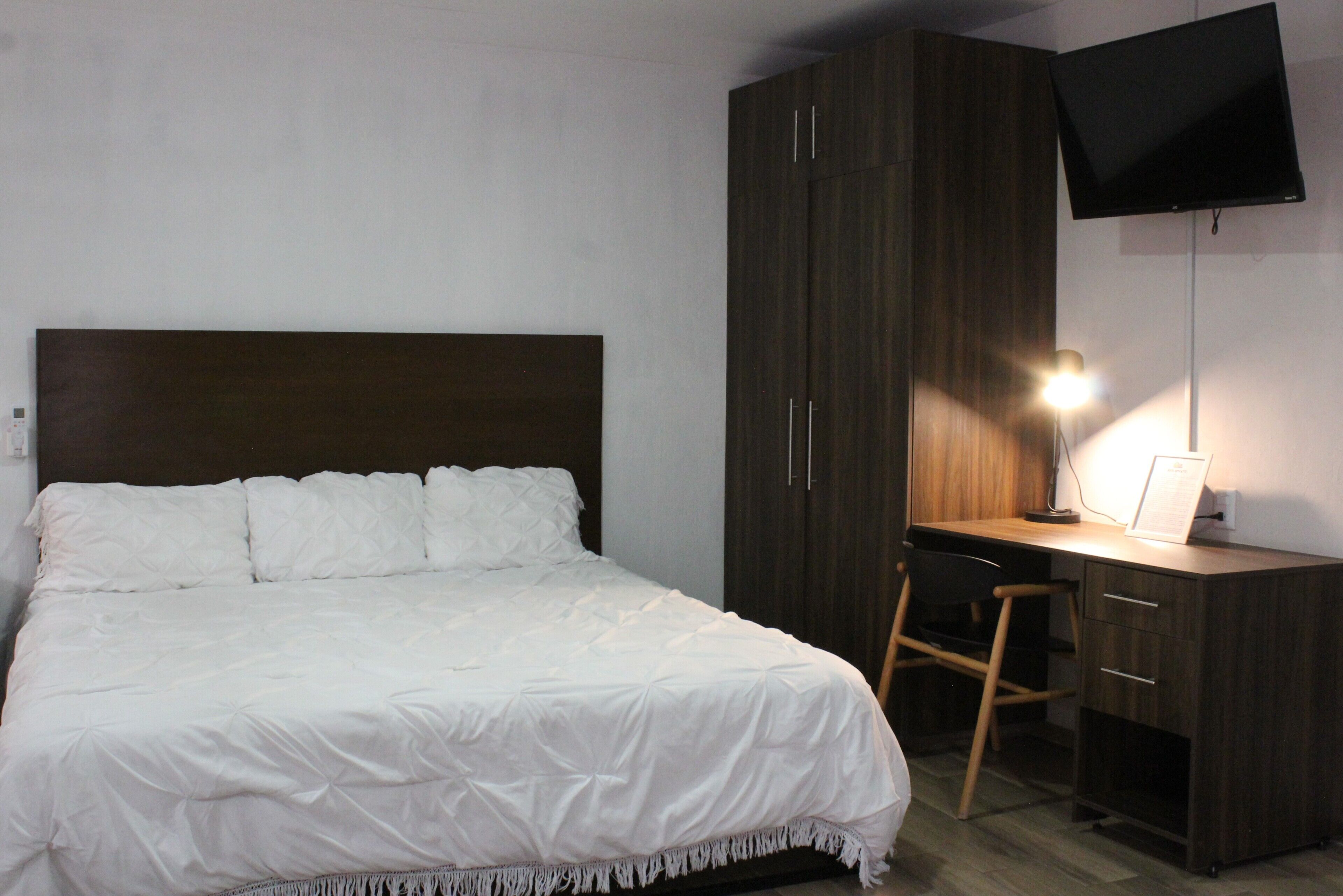 Une chambre à coucher avec un lit, un bureau, une chaise, une télévision et une lampe.