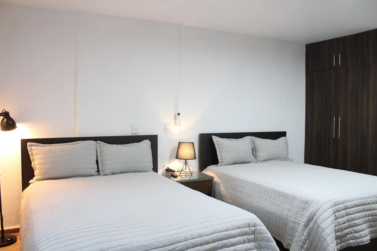 A hotel room with two beds, a nightstand with a lamp, and a wardrobe.