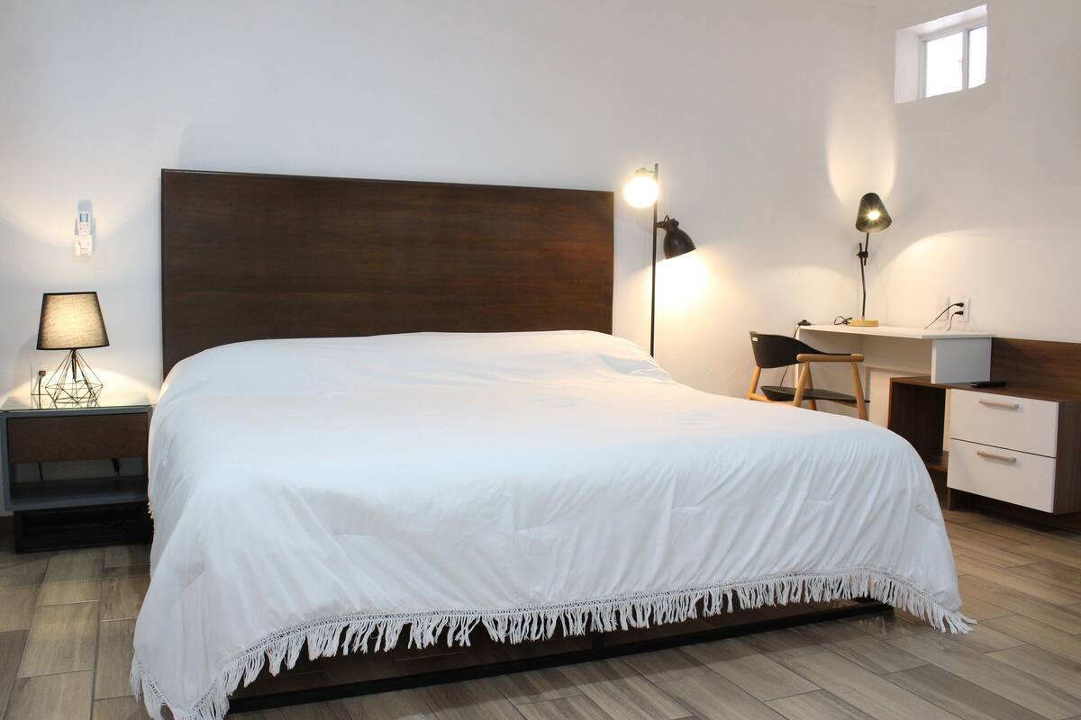 A neatly arranged bedroom with a large bed, bedside lamps, a desk, and a chair.