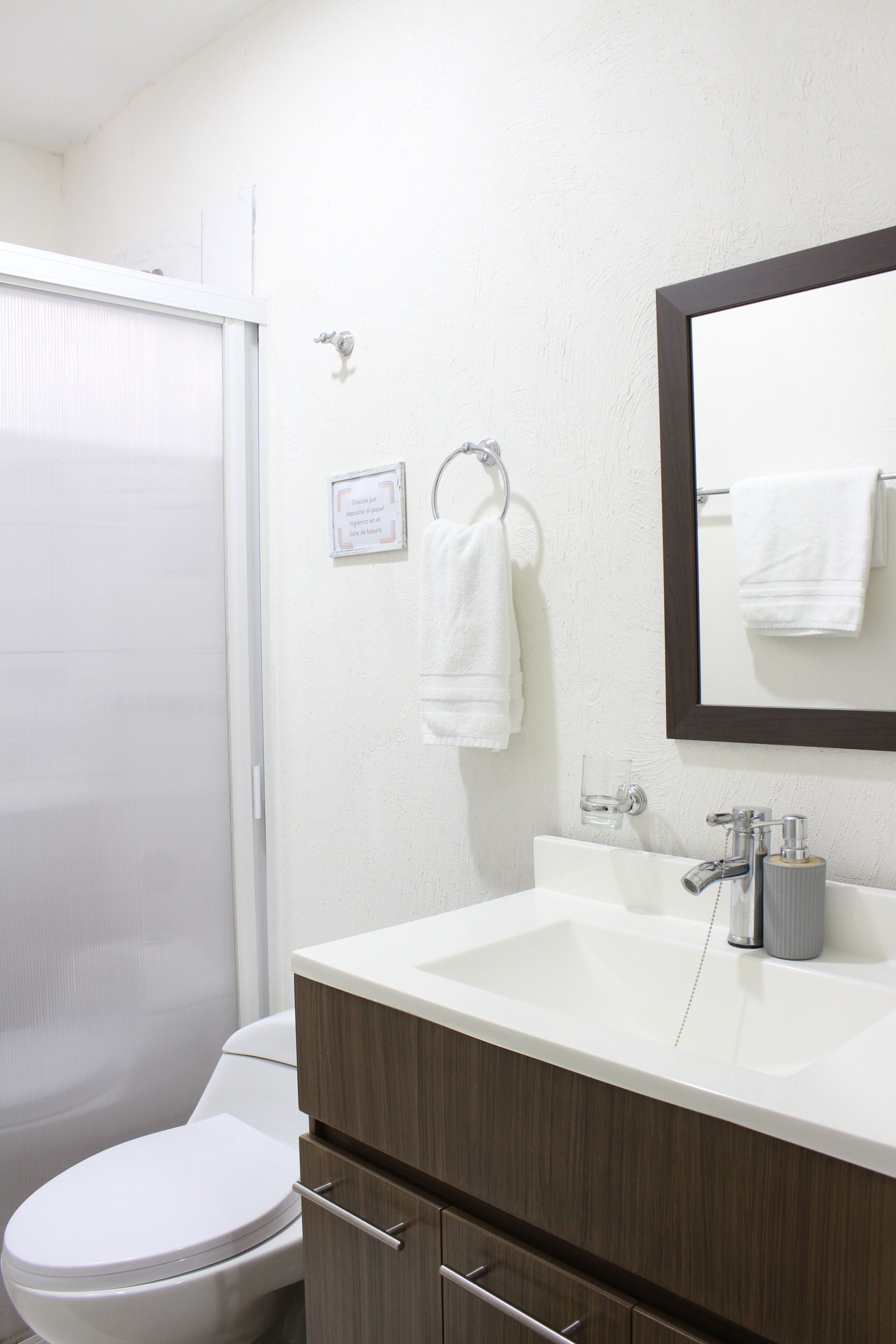 Un bany amb un vàter blanc, un lavabo amb un mirall a sobre i una tovallola penjada a un suport.