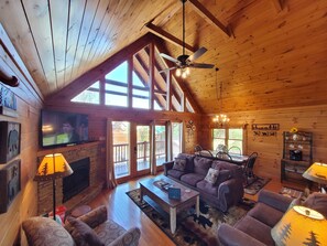 Un salón amplio con techo alto, vigas de madera, chimenea, televisor y comedor con mesa y sillas.