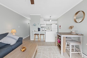 Un espacio habitable compacto con kitchenette, sofá, mesa de centro y zona de comedor con taburetes.