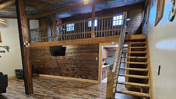 Une pièce spacieuse avec un plancher en bois, un ventilateur de plafond et un escalier menant à un niveau supérieur.