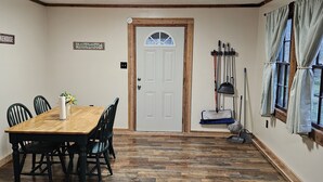 Un coin repas avec une table et des chaises en bois, une porte blanche et un balai appuyé contre le mur.