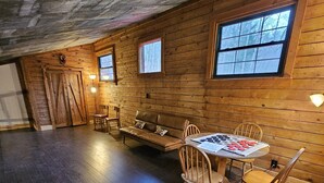 L’intérieur d’une cabane en rondins, avec un plancher en bois foncé, un banc en bois, une table avec des chaises et une fenêtre donnant sur la forêt.