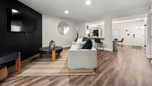 Ein modernes Wohnzimmer mit Flachbildfernseher, rundem Spiegel, Sofa und Couchtisch.