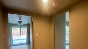 A hallway with wooden flooring, a ceiling fan, and a door leading to a balcony.