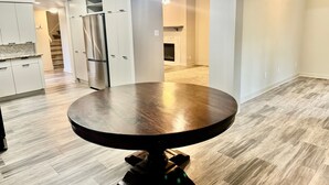 A modern kitchen with white cabinetry, a stainless steel refrigerator, and a round dining table with a dark wood top.