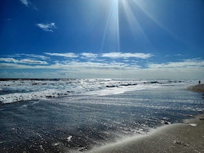A beach with waves, a clear sky, and a person walking.