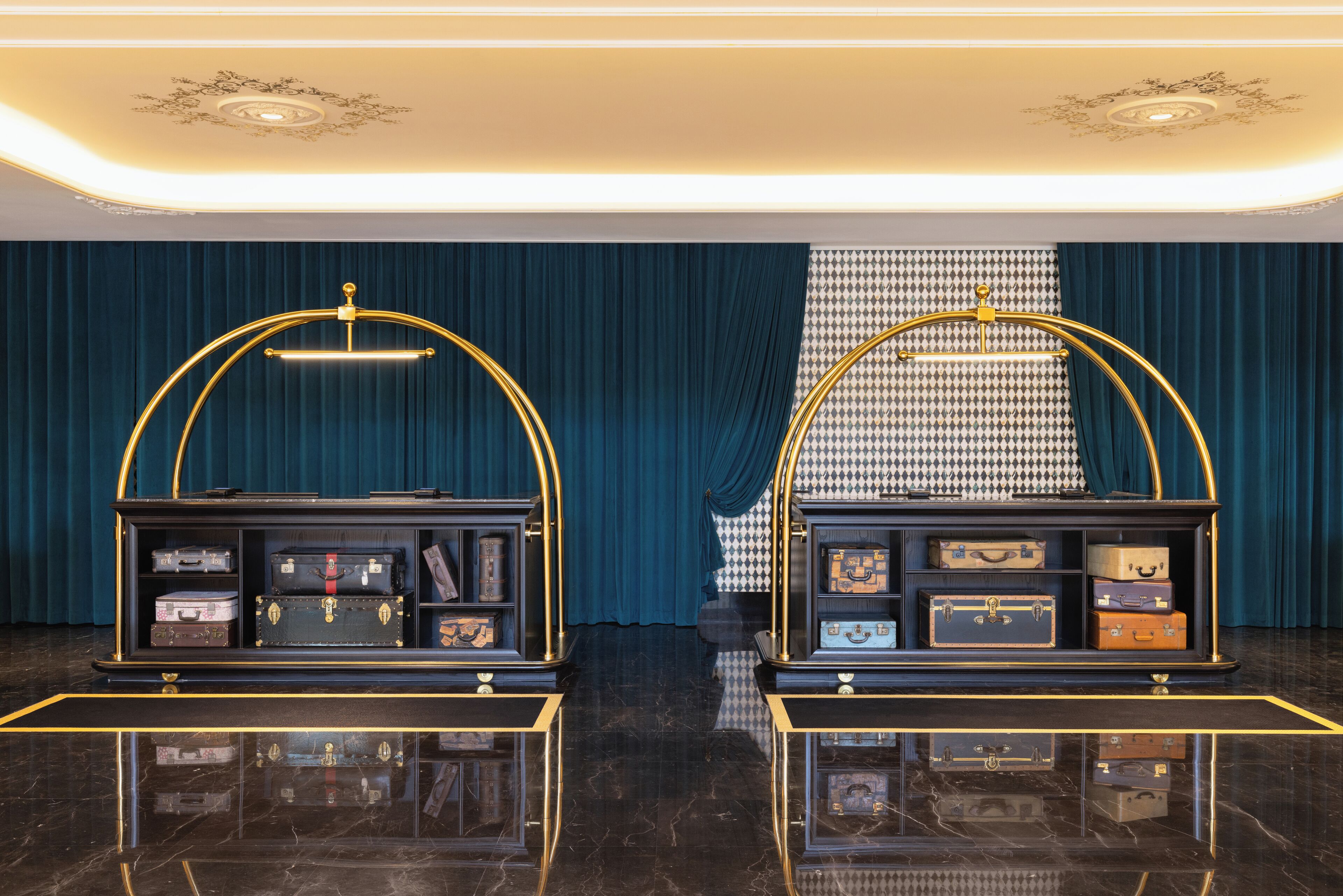 A luxurious room with a dark blue curtain backdrop, a patterned wall, and two display cases with vintage suitcases.