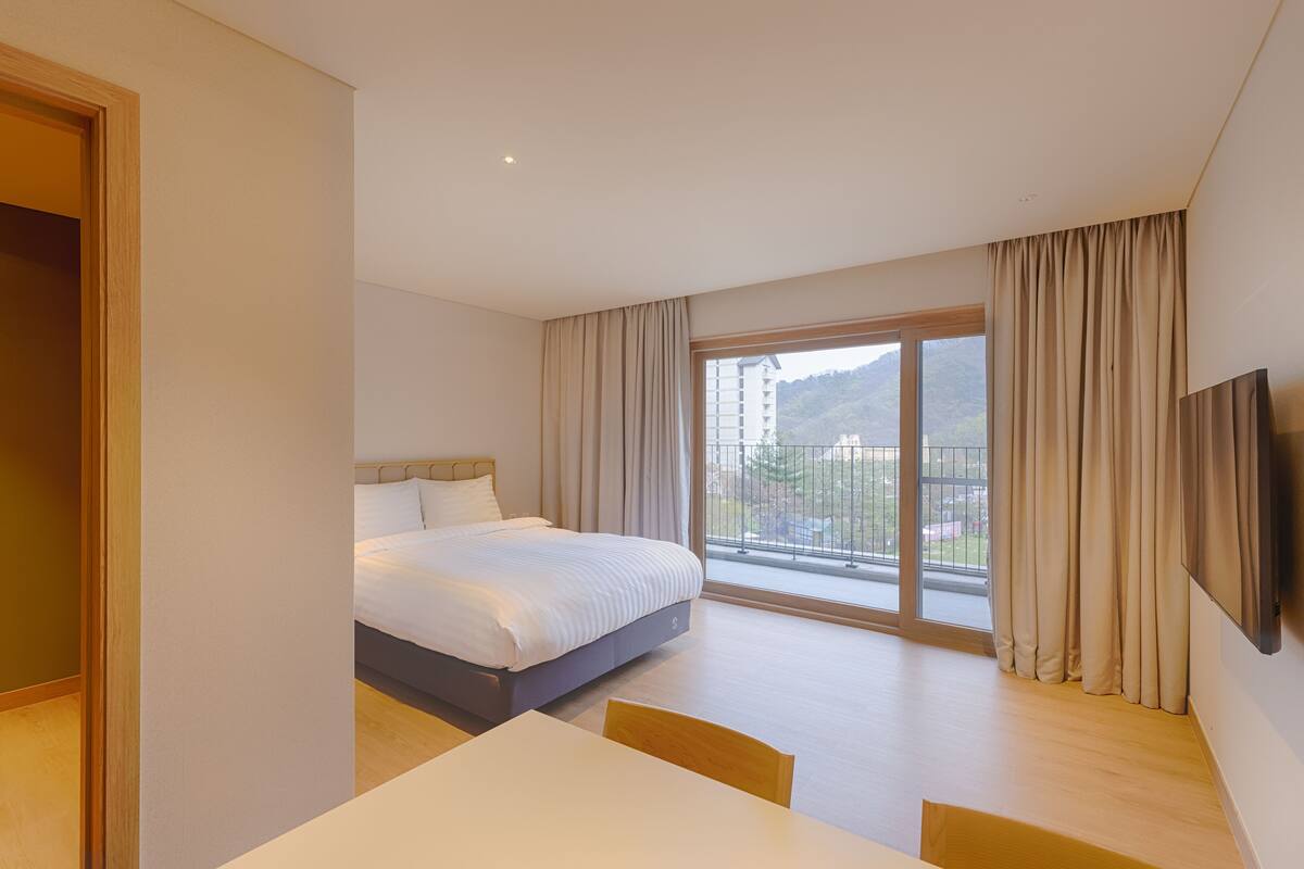 A hotel room with a bed, a dining table, and a large window with curtains.